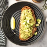 spicy avocado bread toast garnished with avocado cubes, served in a plate with lime wedges.