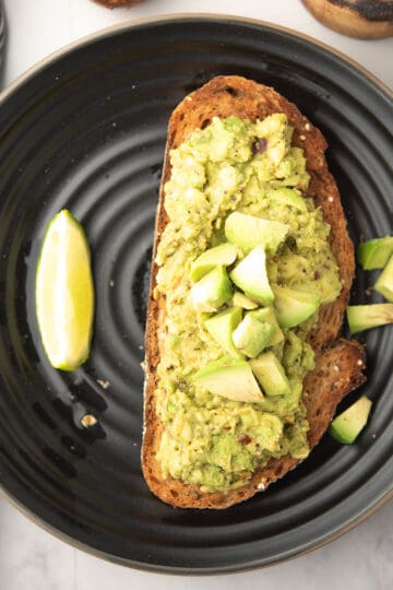 spicy avocado bread toast garnished with avocado cubes, served in a plate with lime wedges.
