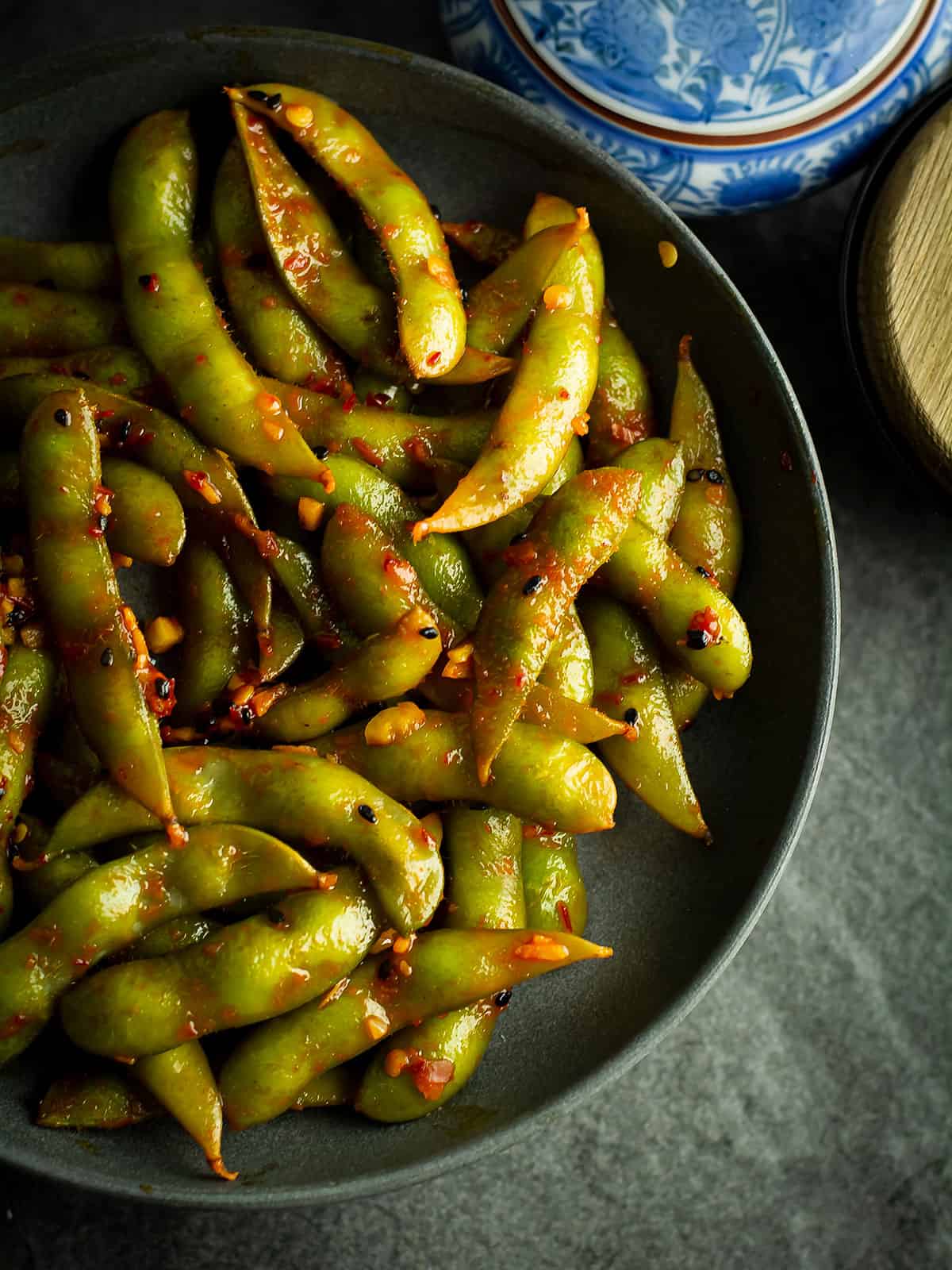 Close-up of spicy garlic edamame, glistening with garlic and chili sauce.