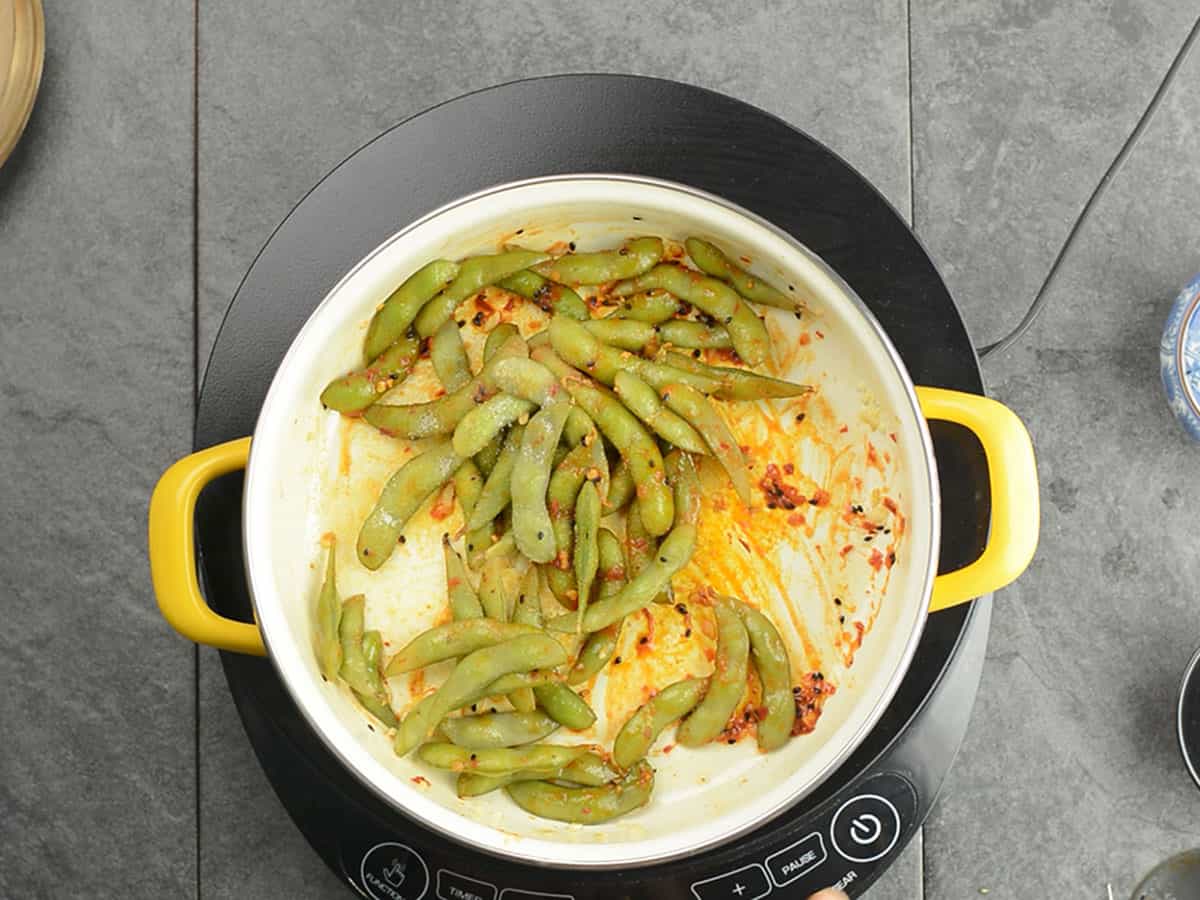 Tossed edamame coated with the spices in the pan
