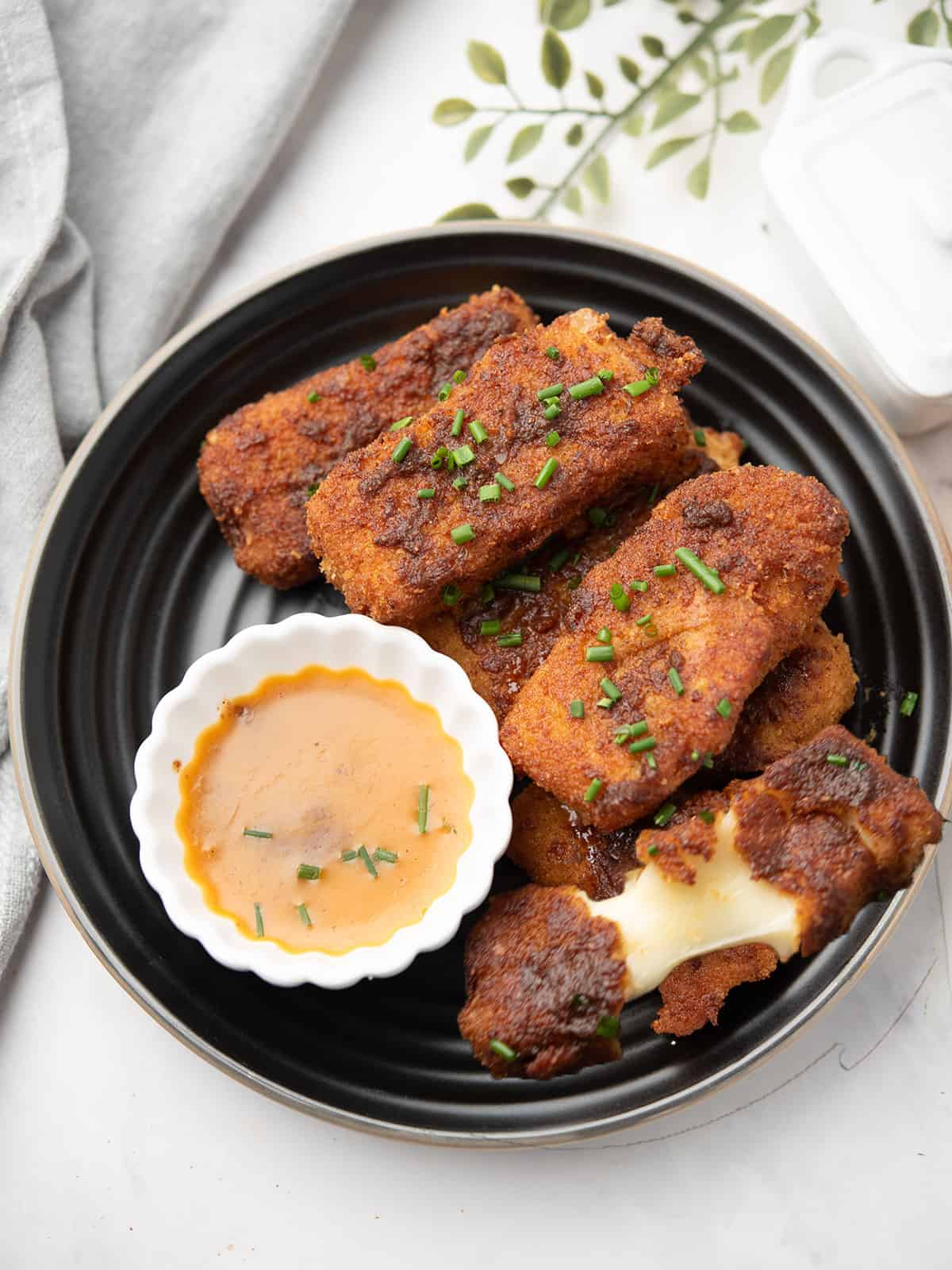 Golden brown Nashville Hot Mozzarella Sticks garnished with herbs and a dipping sauce served on a plate.