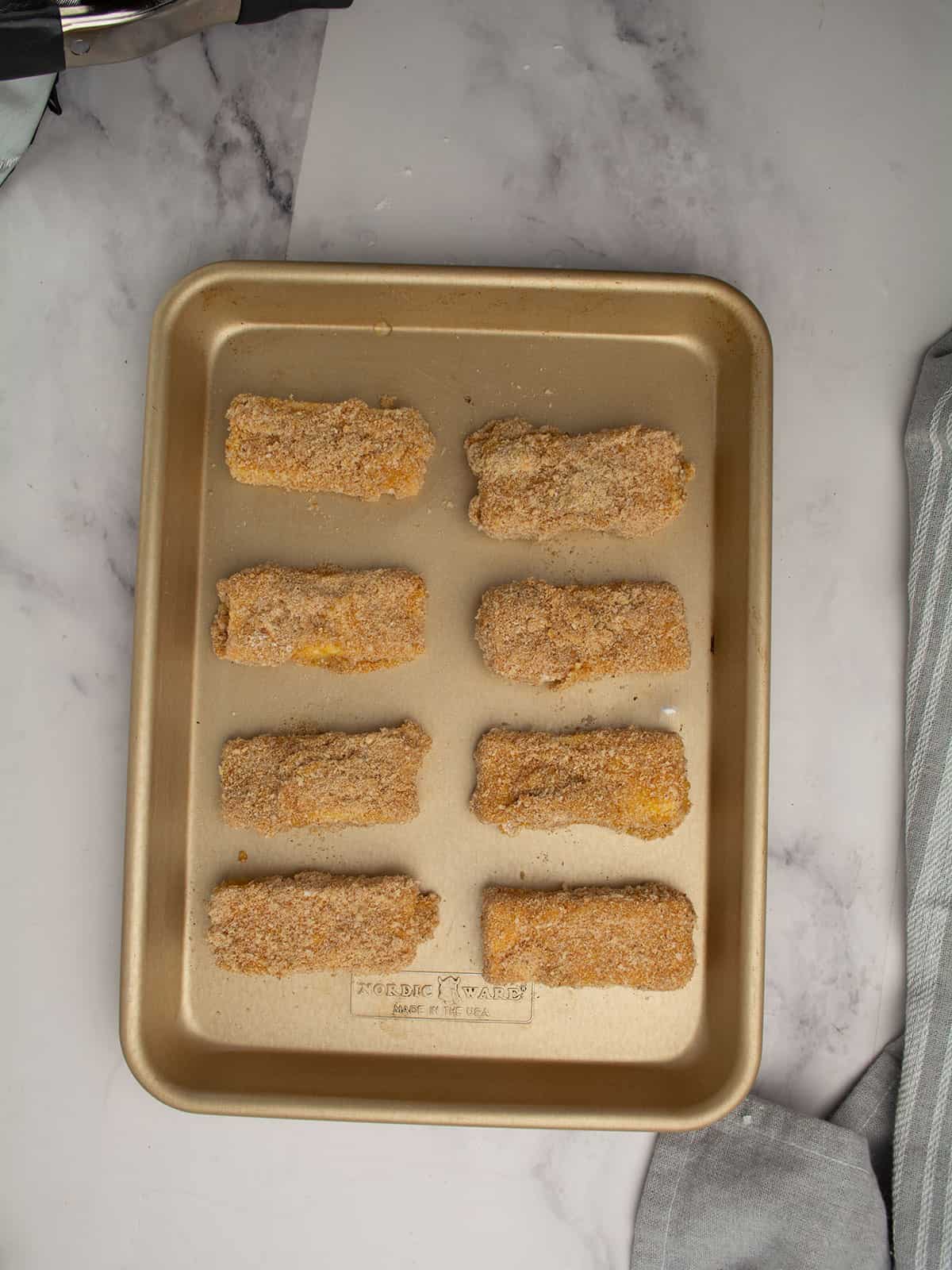 breaded mozzarella sticks arranged in a baking tray.
