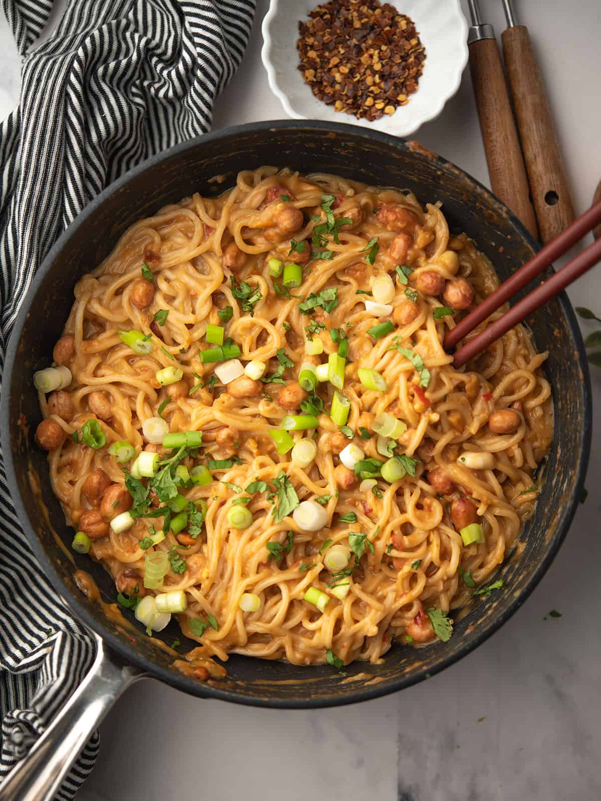 A pan of Chili Peanut Noodles topped with green onions and crushed peanuts.