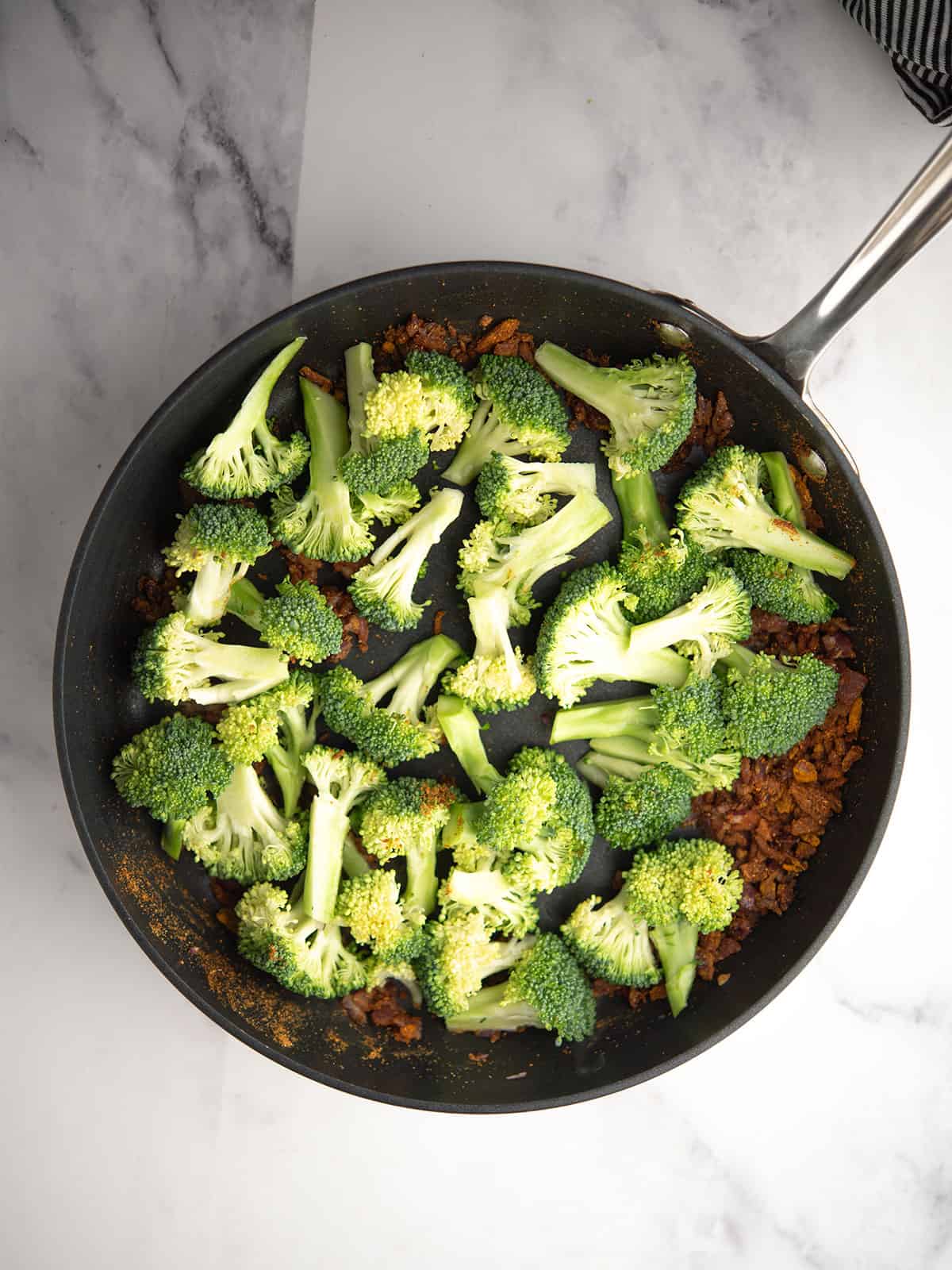 Steaming broccoli florets with spices in a covered pan.