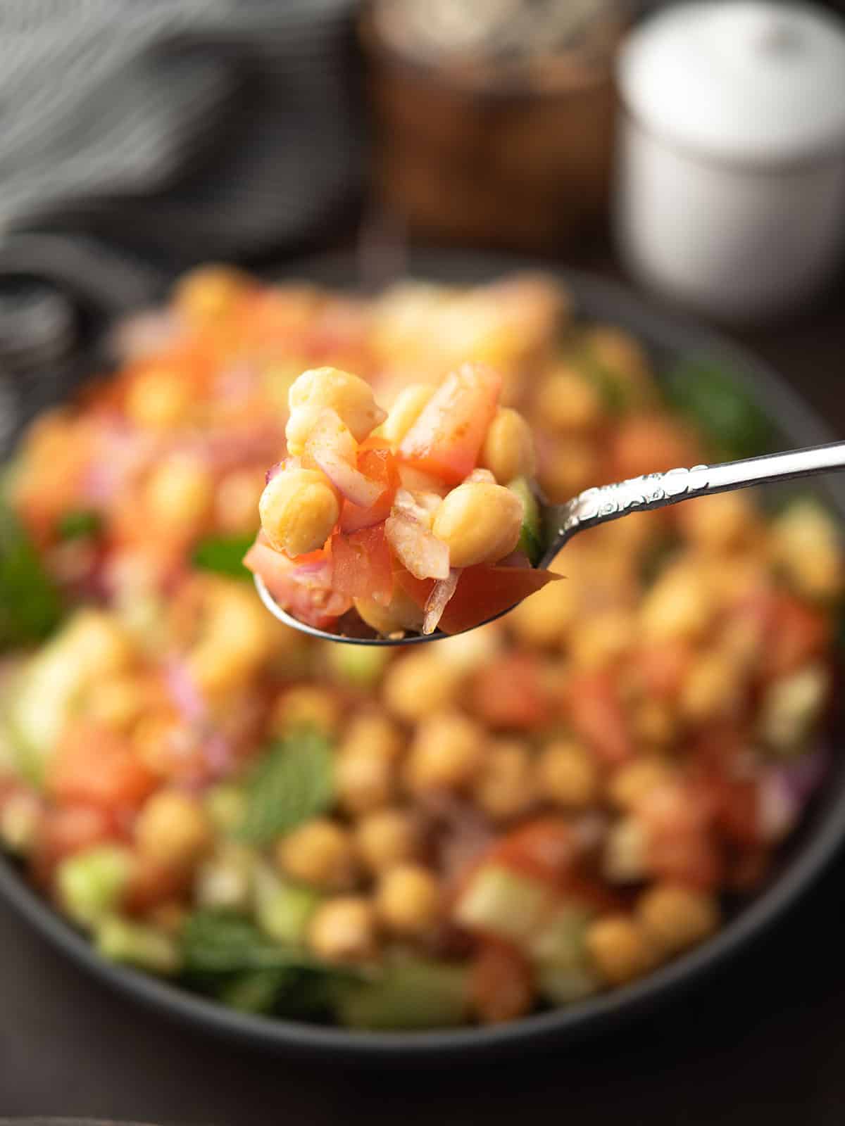 Indian chickpea salad in the spoon along with tomato and spoon.