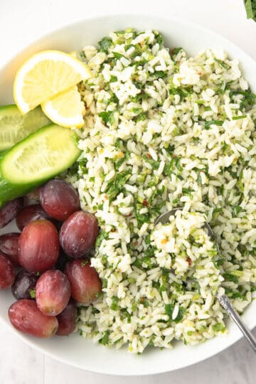Delicious chimichurri rice served in a bowl with spoon, garnished with lemon slices and cucumber.