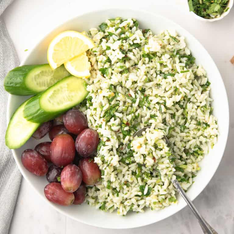 Delicious chimichurri rice served in a bowl with spoon, garnished with lemon slices and cucumber.