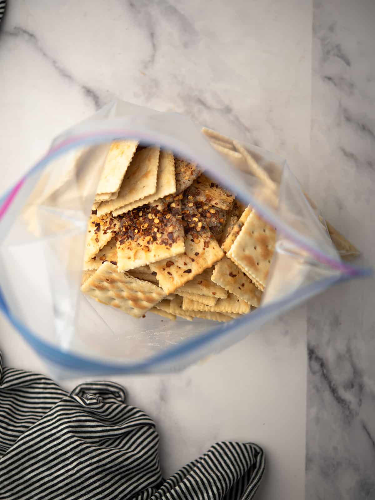 Pouring seasoned oil over Saltine crackers in a bag.