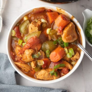 Cajun chicken stew loaded with vegetables and garnished with green onion, served in a bowl.