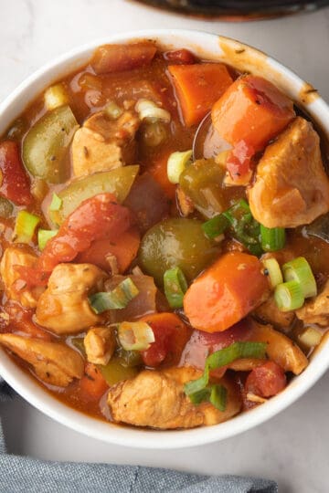 Cajun chicken stew loaded with vegetables and garnished with green onion, served in a bowl.