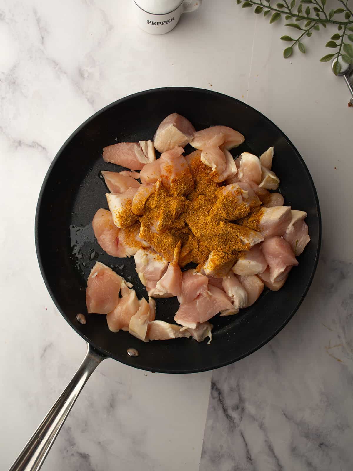 Chunks of chicken seasoned with Cajun spices in a skillet.