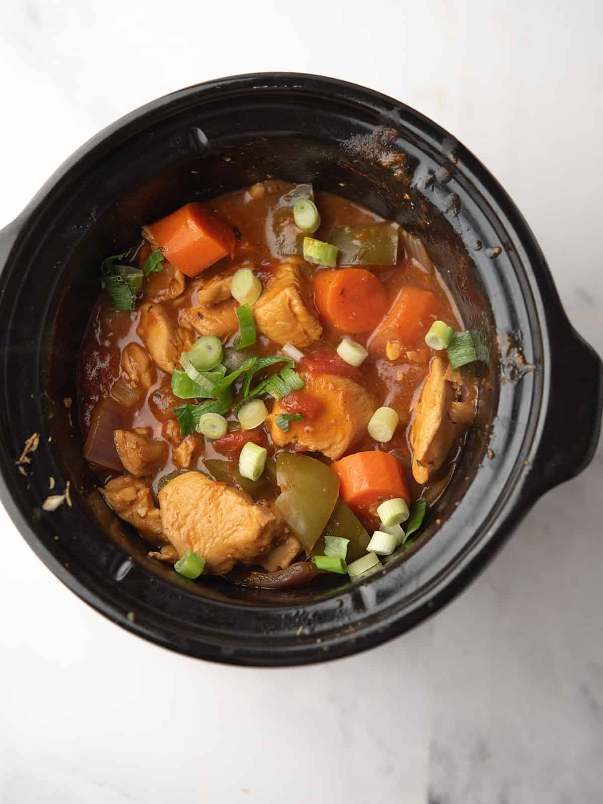 A close-up of Cajun chicken stew served with rice and herbs on top in the slow cooker