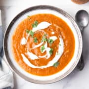 roasted red pepper and tomato soup in the white serving bowl with the spoon, garnished with cream and herbs
