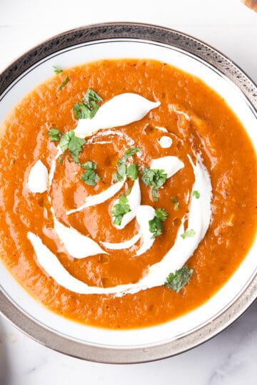 roasted red pepper and tomato soup in the white serving bowl with the spoon, garnished with cream and herbs