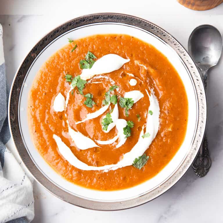 roasted red pepper and tomato soup in the white serving bowl with the spoon, garnished with cream and herbs