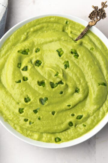 Close-up of vibrant green avocado cream sauce ready to serve over taco in a small white bowl