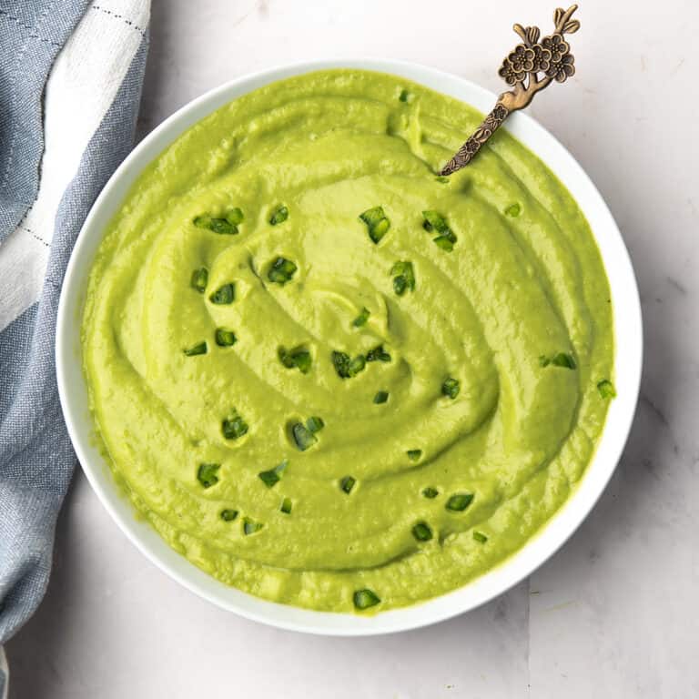 Close-up of vibrant green avocado cream sauce ready to serve over taco in a small white bowl