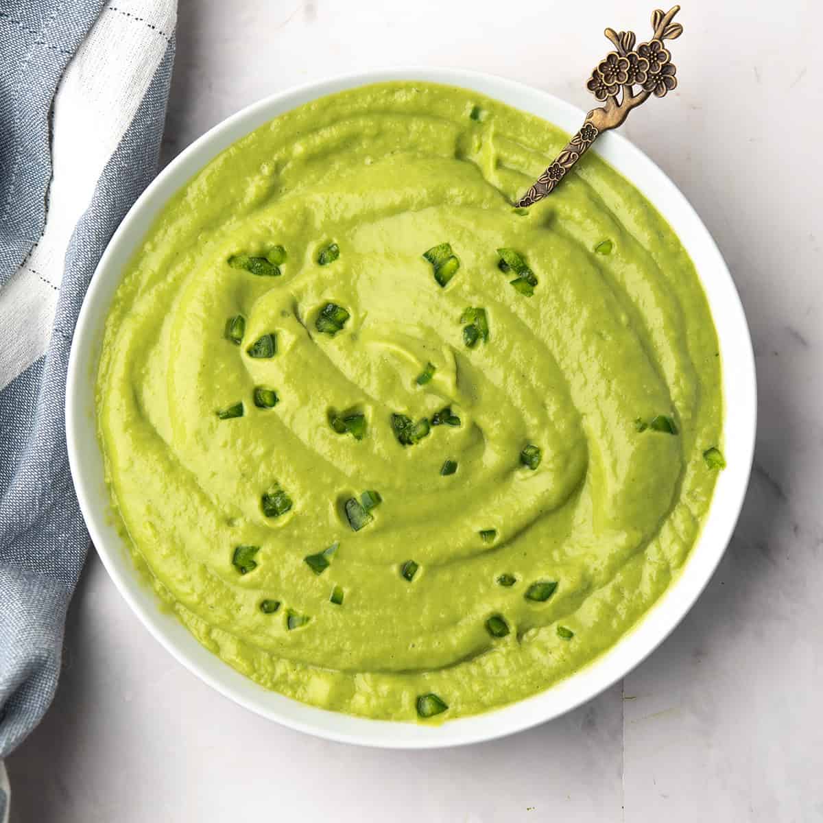 Close-up of vibrant green avocado cream sauce ready to serve over taco in a small white bowl