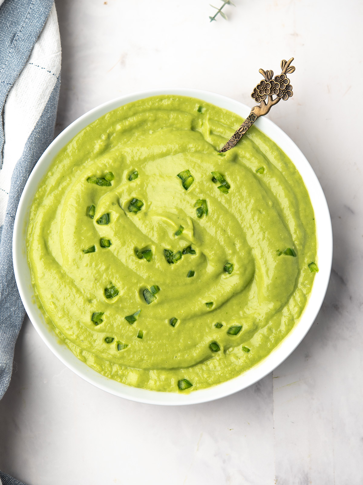 Bowl of creamy avocado cream sauce with jalapeño and cilantro garnish to drizzle over taco