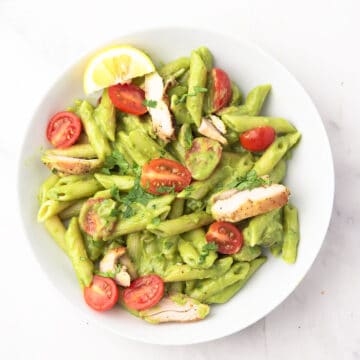 Creamy avocado pasta with grilled chicken on a white dinner bowl