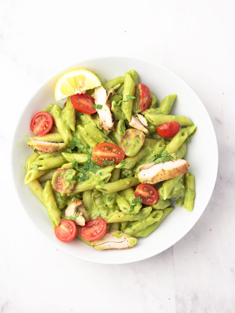 Creamy avocado pasta with grilled chicken on a white dinner bowl