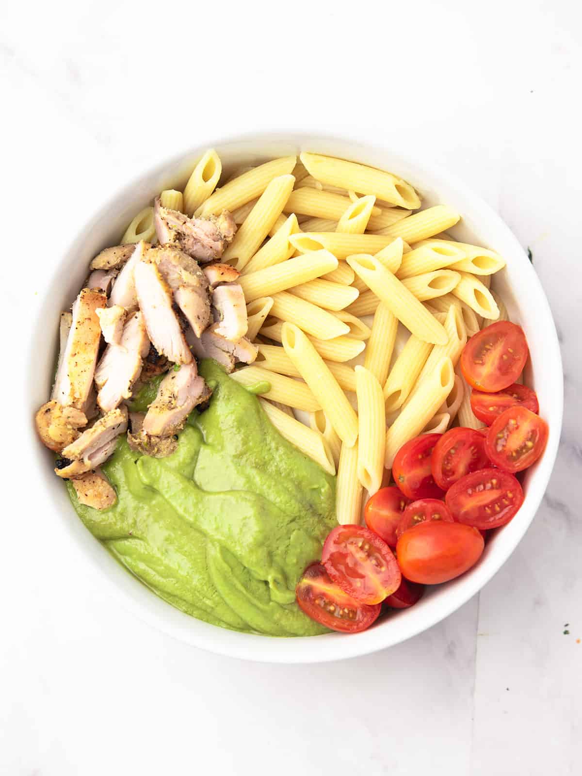 avocado sauce, pasta, chicken, and cherry tomatoes placed in a bowl