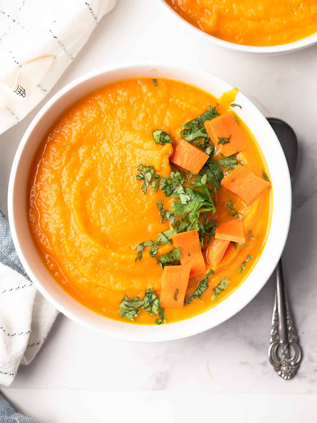 Carrot apple ginger soup topped with fresh cilantro served in the dinner table with a spoon.