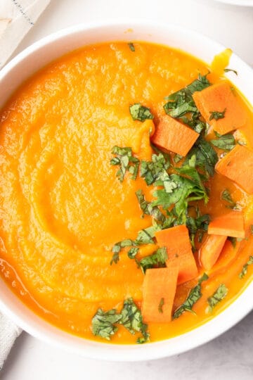 carrot apple ginger soup served in a bowl garnished with cilantro and ready to serve for the weekend dinner.