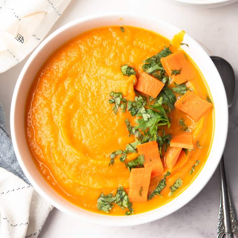 carrot apple ginger soup served in a bowl garnished with cilantro and ready to serve for the weekend dinner.