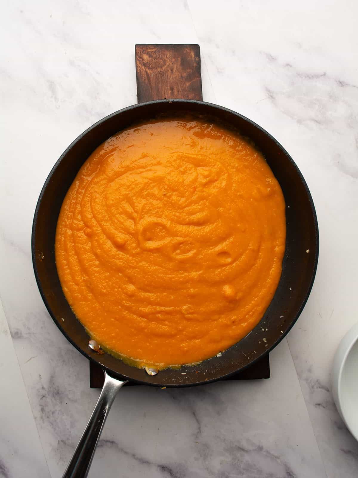 Blending carrot apple ginger soup to a smooth consistency with an immersion blender.