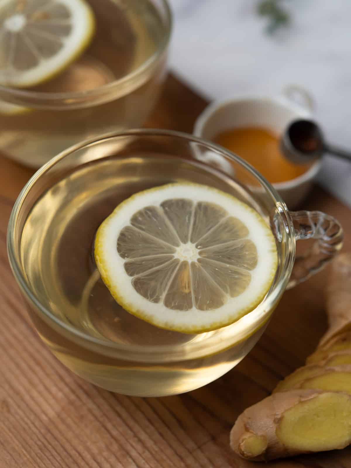 Warm ginger lemon honey tea in a clear glass on a wooden table.