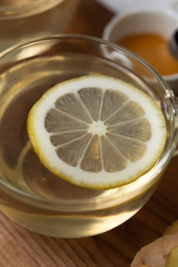 Comforting ginger lemon honey tea with ingredients in the background.
