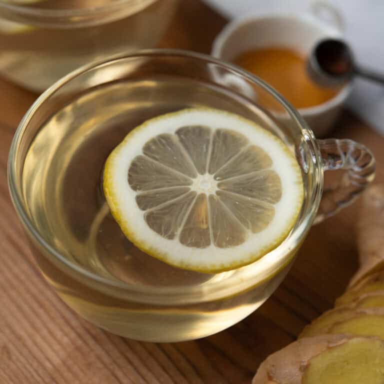 Comforting ginger lemon honey tea with ingredients in the background.