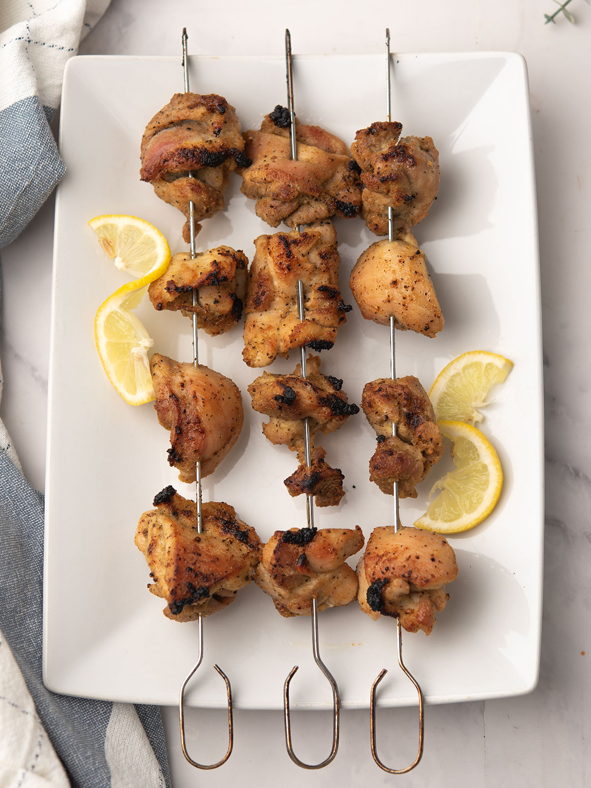 Beautifully plated lemon pepper chicken skewers on a white serving platter.