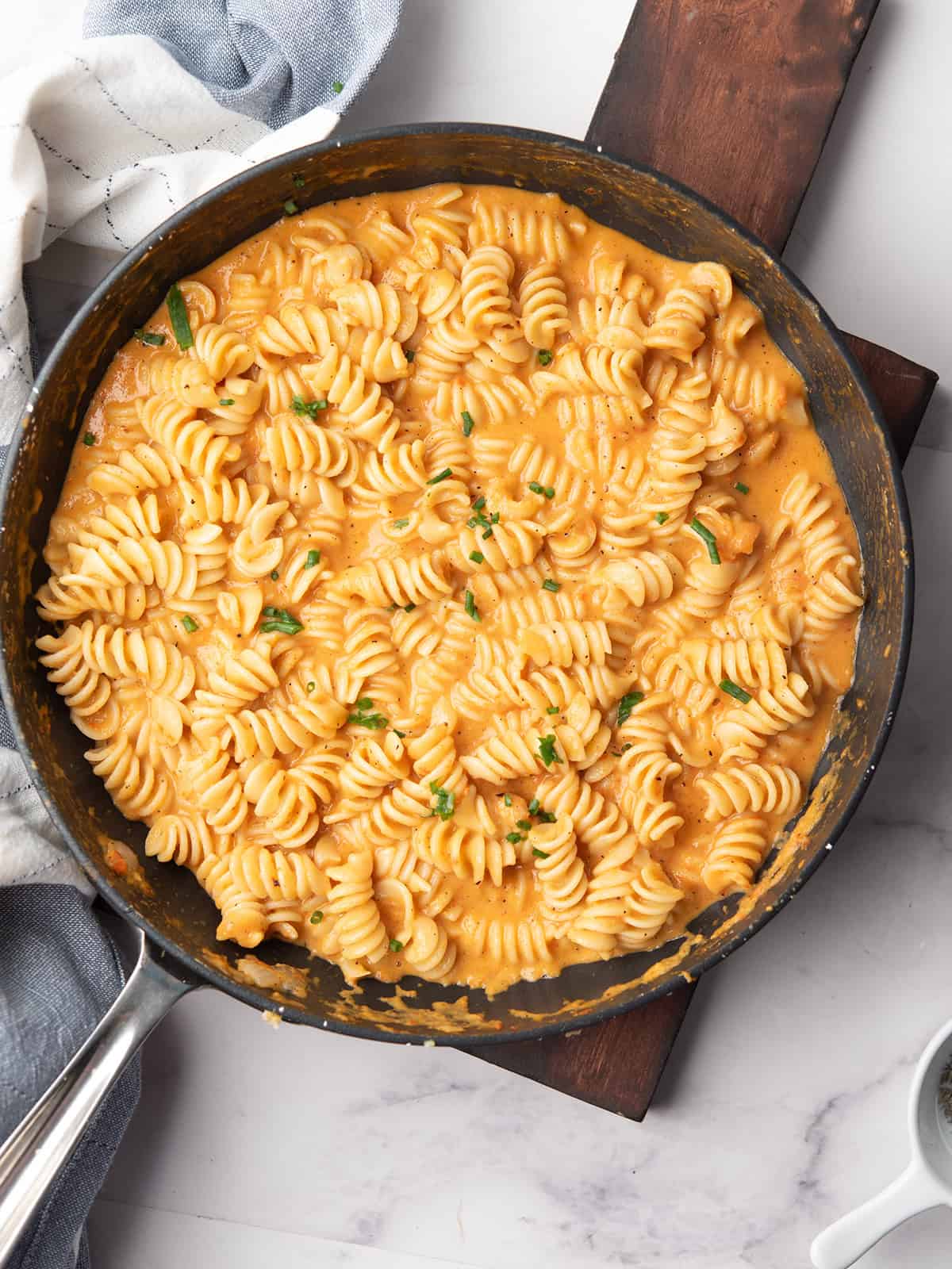 A pan of creamy red pepper pasta topped with grated Parmesan and fresh herbs