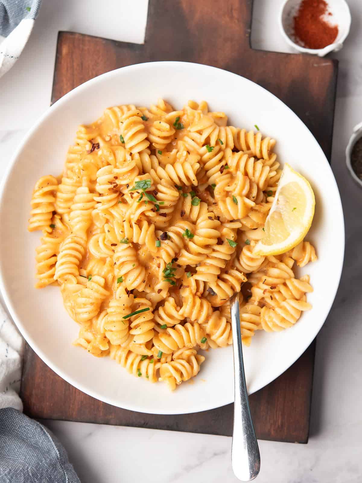 A close-up view of creamy red pepper pasta with roasted red peppers, served in a plate with fork at the dinner table.