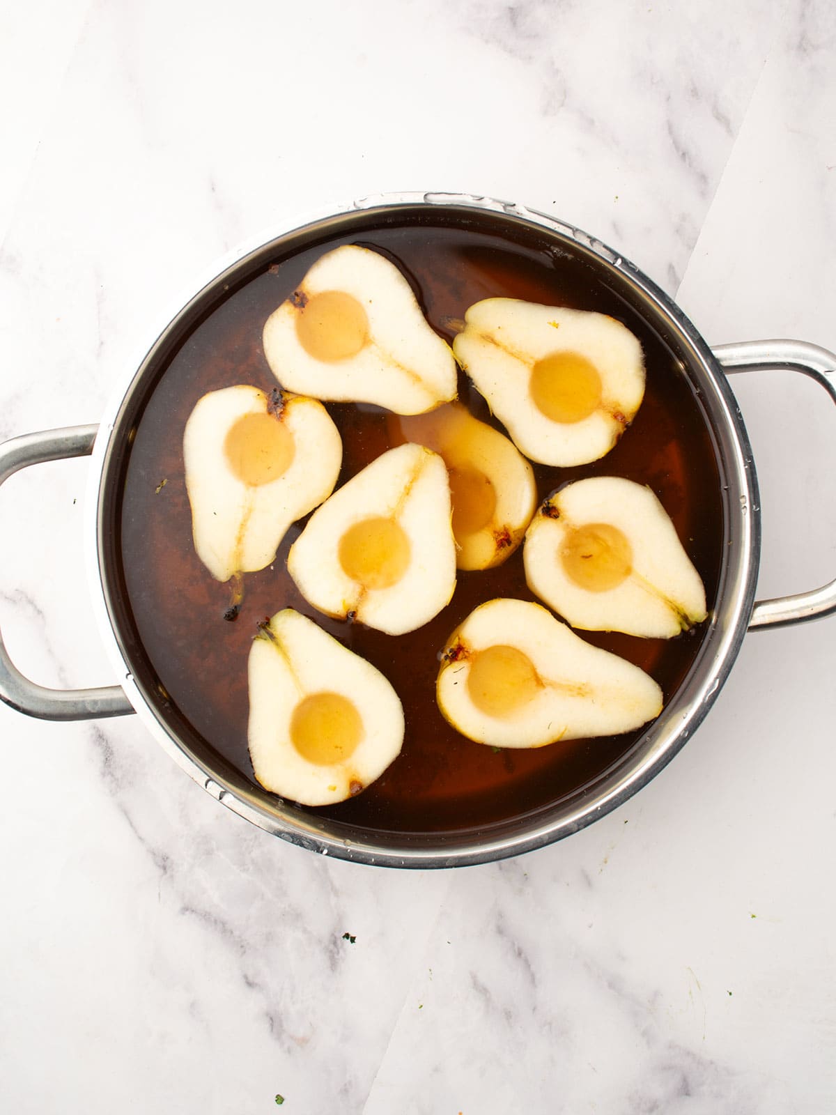 Adding pear halves into the simmering syrup in the pot.
