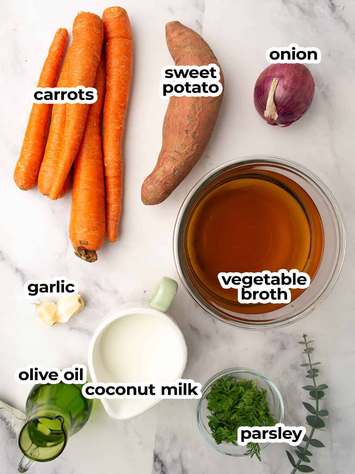 carrots, sweet potato, onion, garlic, and herbs on a table ready to make sweet potato and carrot soup