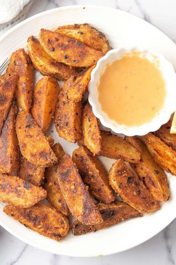spicy potato wedges are looking crispy and golden brown served with dipping sauce.