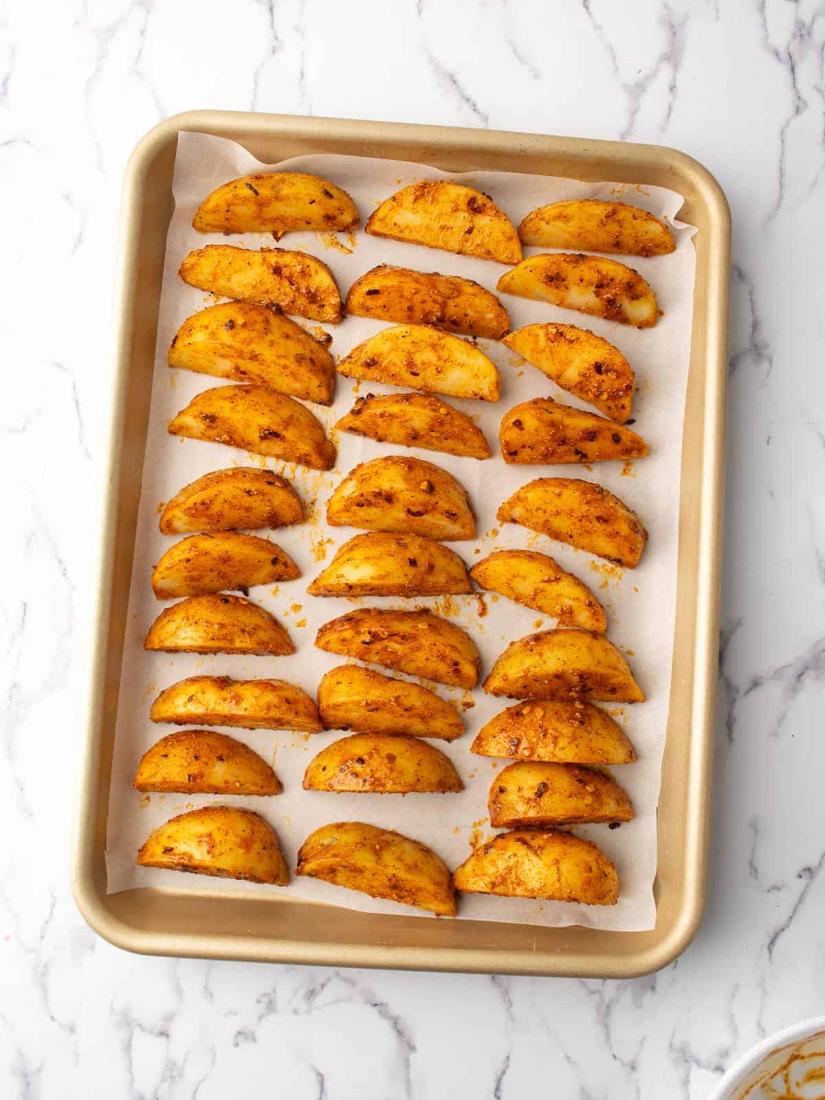 spicy potato wedges are arranged in the baking tray.