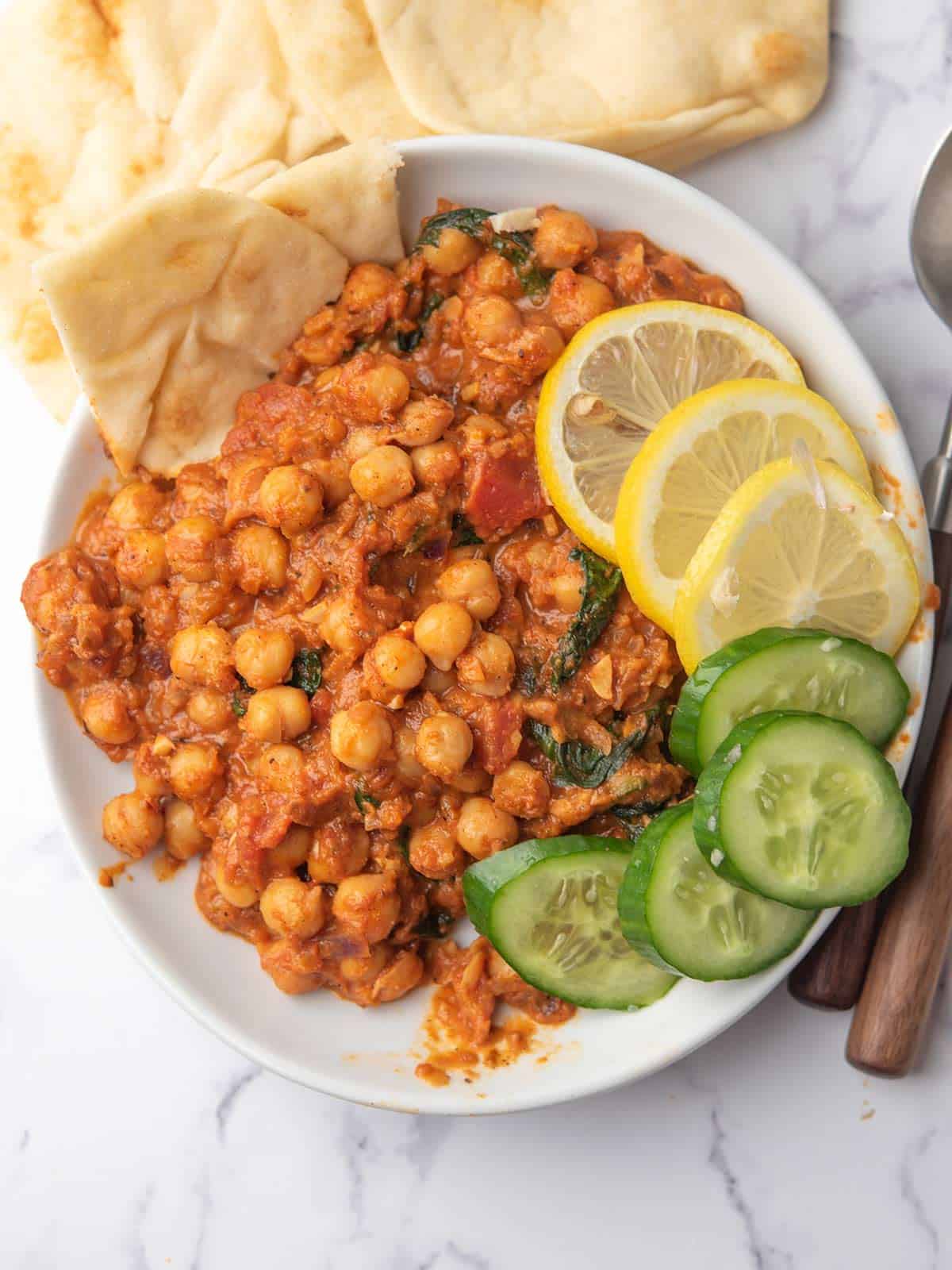 creamy harissa chickpeas served with naan bread and lemon slices.