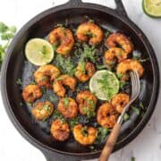 chili lime shrimp in a cast iron pan served with lime wedges and cilantro garnish.