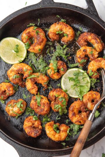 chili lime shrimp in a cast iron pan served with lime wedges and cilantro garnish.