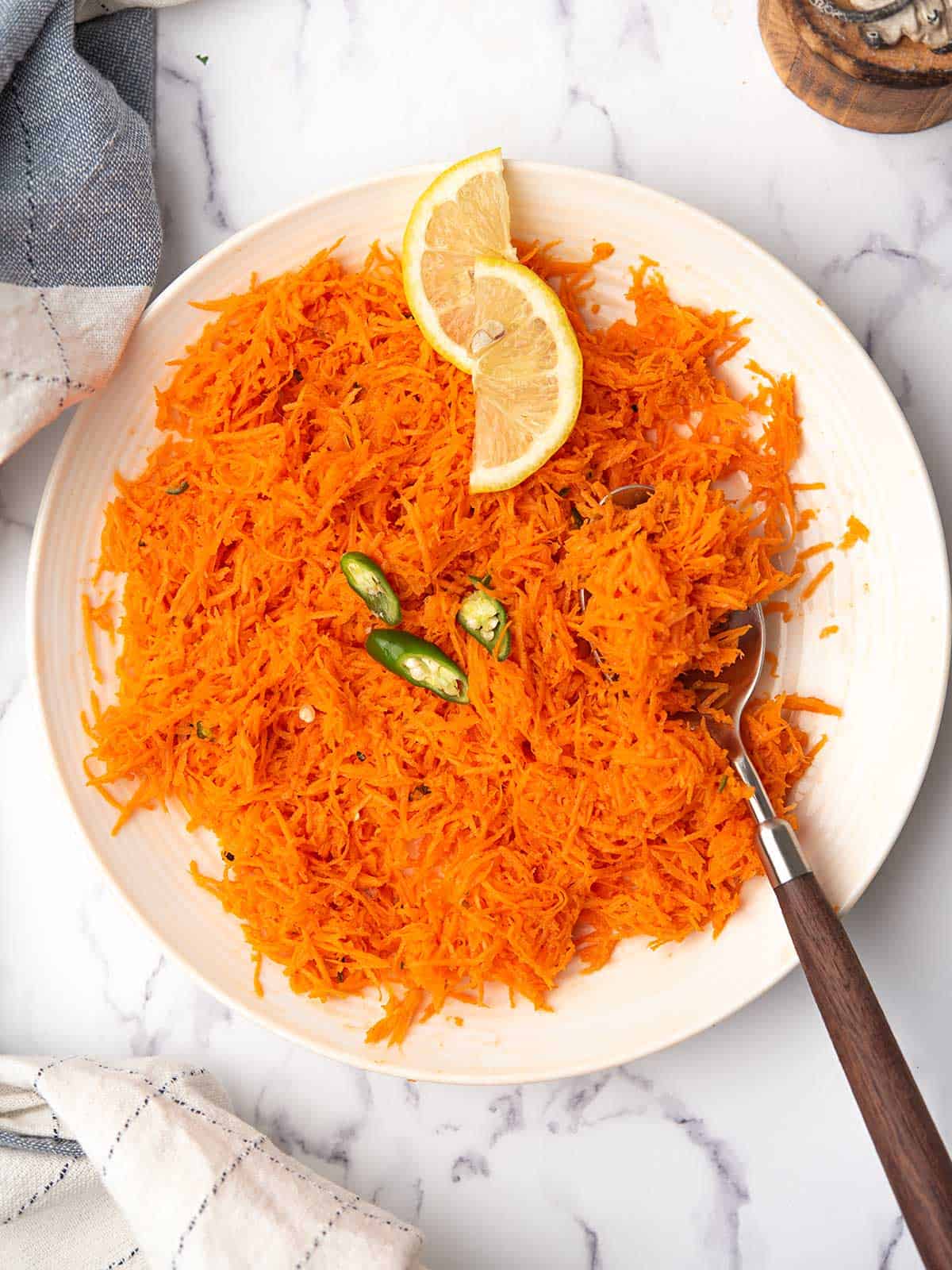 indian carrot salad in a white serving bowl garnished with lemon slices and serrano pepper slices.