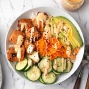 the spicy salmon bowl served in a dinner bowl garnished with sesame seeds and teh spicy sriracha mayo.