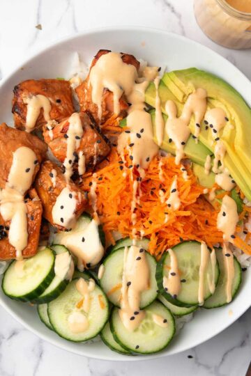 the spicy salmon bowl served in a dinner bowl garnished with sesame seeds and teh spicy sriracha mayo.