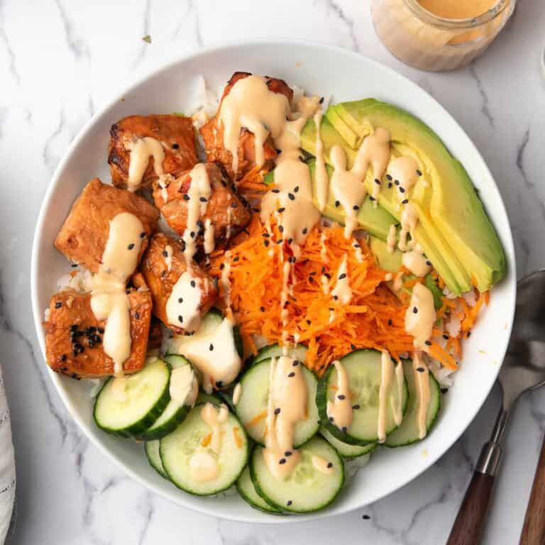 the spicy salmon bowl served in a dinner bowl garnished with sesame seeds and teh spicy sriracha mayo.