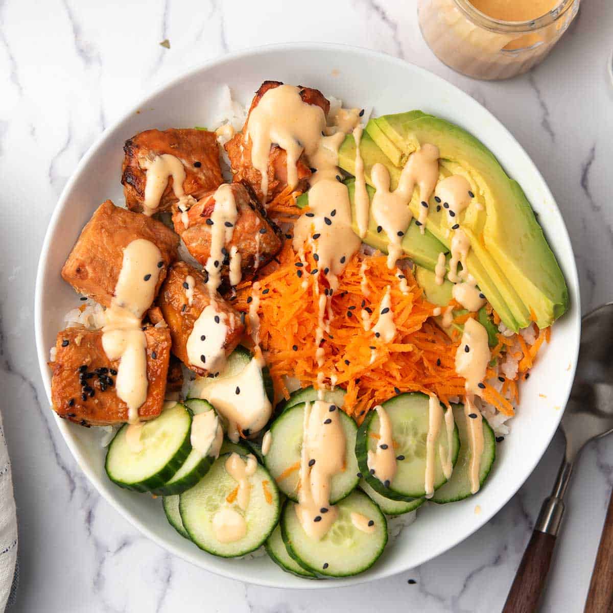 the spicy salmon bowl served in a dinner bowl garnished with sesame seeds and teh spicy sriracha mayo.