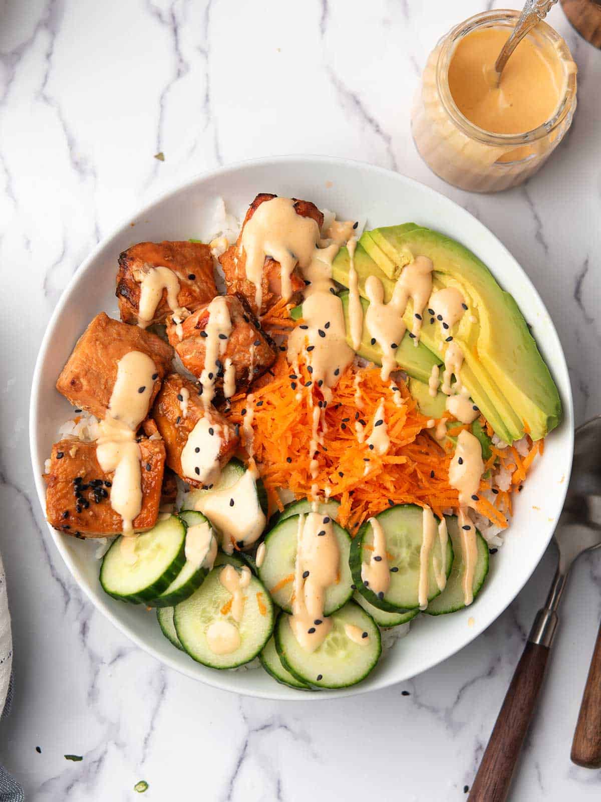 The spicy salmon bowl served in the dinner table with cucumber, carrot, avocado and homemade sriracha sauce.
