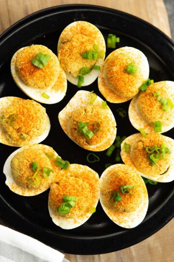 Cajun deviled eggs garnished with green onion, served in a black plate for the party,